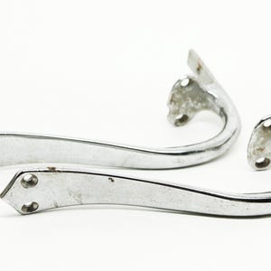 May include: Two chrome-plated metal door handles with a curved design. The handles are in a close-up view and are arranged in a way that they are overlapping each other.