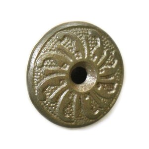 May include: A round, metallic, decorative knob with a floral design. The knob is a light brown color and has a small hole in the center.