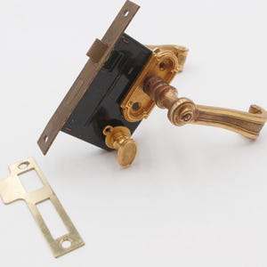 May include: An antique door lock set with a brass finish. The set includes a rectangular black and brass lock body, a matching door handle, a small oval knob, and a separate strike plate. The hardware is likely for a vintage door.