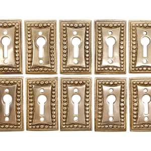 May include: Ten antique brass keyhole escutcheons with a beaded border. Each escutcheon has a keyhole in the centre and a decorative design around the edges.