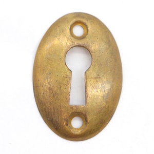 May include: A brass keyhole cover with an oval shape and two small holes on the sides. The keyhole is in the center of the cover.