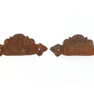May include: Two antique, ornate, cast iron drawer pulls with intricate floral designs. The pulls are rusty brown and have a square shape with a decorative edge.