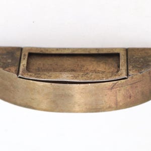 May include: A vintage, semi-circular brass box with a rectangular compartment in the centre. The box has a hinged lid and a tarnished, aged appearance, suggesting it is an antique or a well-loved item.
