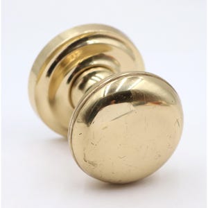 May include: A close-up of a brass doorknob with a round, polished design. The doorknob has a circular base and a rounded handle, showing signs of wear. The hardware is a warm gold color.