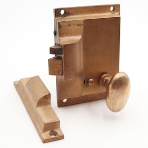 May include: A vintage brass door lock set with a rectangular body, an oval knob, and a separate strike plate. The lock has a warm, aged patina, suggesting its antique nature. The set is designed for mortise installation.