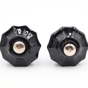 May include: Two black, star-shaped cabinet knobs with a silver center. The knobs have a glossy finish and are set against a white background. These decorative knobs are suitable for furniture restoration or DIY projects.