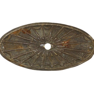 May include: An oval-shaped, metal, decorative plate with a sunburst design. The plate is a dark brown colour with a slightly rusted appearance.