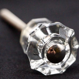 Può includere: Una maniglia per porta in vetro trasparente con un gambo in metallo argentato. La maniglia ha un design sfaccettato e un centro rotondo in metallo argentato.