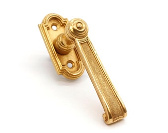 May include: A gold-toned door handle with a decorative, ornate design. The handle has a long, rectangular lever with a rounded knob at the top.