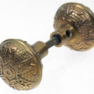 May include: Antique brass door knob with intricate embossed floral and geometric patterns. The knob features a round shape with a detailed design, showcasing a vintage aesthetic. The door knob is a classic hardware piece.