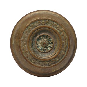 May include: A round, brass door knob with a decorative, concentric circle design. The knob has a dark patina and a raised, circular center.