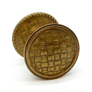 May include: A pair of antique brass door knobs with a woven pattern. The knobs are round and have a raised edge.
