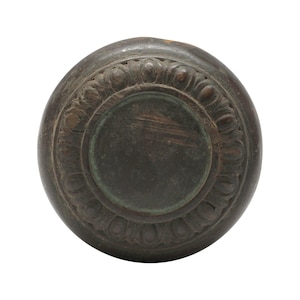 May include: A round, dark brown wooden knob with a decorative, carved design around the edge. The knob has a slightly raised, circular centre.