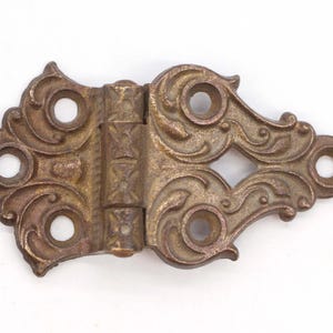 May include: Ornate brass hinge with a decorative, floral design. The hinge has multiple holes and a textured surface.