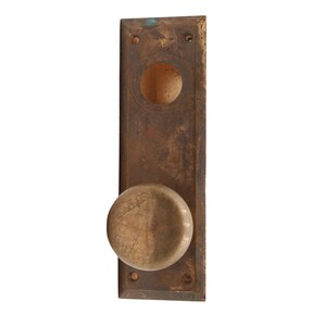May include: A brass door knob with a round, slightly domed shape. The knob is attached to a rectangular brass plate with a keyhole.