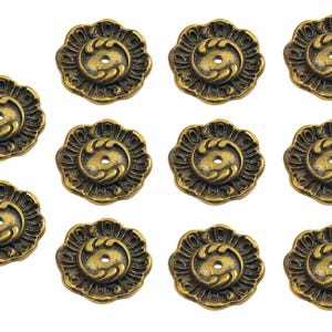 May include: Twelve antique brass-coloured floral cabinet knobs are displayed. Each knob has a detailed, symmetrical design with a central hole and a decorative, petal-like border. The knobs are arranged against a white background.