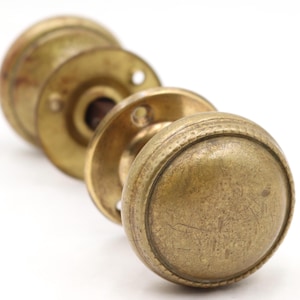 May include: Close-up of antique brass doorknobs. The doorknobs have a round shape with a textured surface and a warm, aged patina. The set includes multiple knobs and backplates, showcasing a vintage aesthetic. Ideal for home restoration projects.