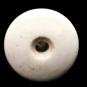 May include: A white ceramic knob with a round shape and a small hole in the center. The knob has a slightly textured surface.