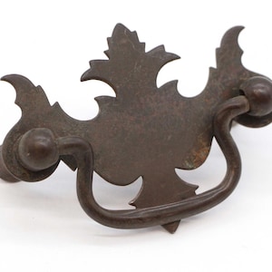 May include: A vintage, ornate, metal drawer pull with a leaf design. The pull is brown and has a slightly tarnished finish.