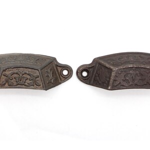May include: Two antique cast iron drawer pulls with a decorative floral design. The pulls are a dark brown color and have a slightly aged appearance.