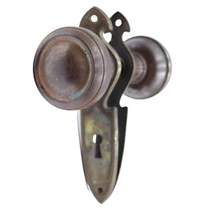 May include: An antique bronze door knob set, featuring a keyhole and decorative backplate. The door knob is round and has an aged appearance. The backplate has an ornate design with a keyhole.