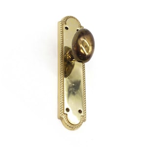 May include: A brass door knob with a rounded design and a decorative plate with a rope-like border.