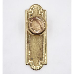 May include: A vintage brass door handle set. The handle features a round knob and a rectangular backplate with decorative edges. The brass has a warm, golden hue and shows signs of age.