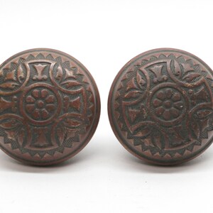 Könnte beinhalten: Zwei antike Türknauf mit Kreuz- und Blumenmuster. Die Knäufe sind aus dunkelbraunem Metall.