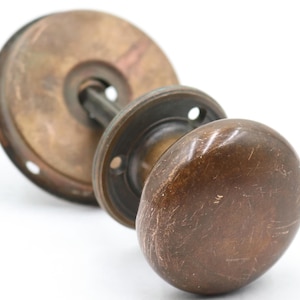 May include: Antique bronze door knob set with a round, oval-shaped knob and a circular backplate. The hardware shows signs of age and wear, with a tarnished finish. The set includes a spindle and mounting hardware.