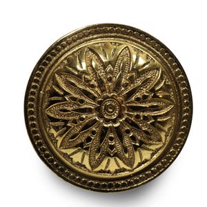 May include: A round, antique-style brass button with an intricate floral design. The button features a detailed, embossed pattern of petals and leaves radiating from a central point, surrounded by a beaded border.