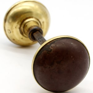 May include: A vintage brass door knob with a brown wooden center. The knob has a decorative design on the brass portion.