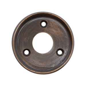 May include: A round, antique brass door knob escutcheon with three screw holes and a center hole for the knob.