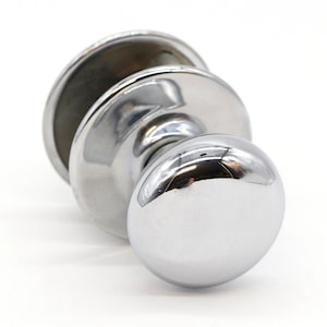 May include: A shiny chrome door knob with a round handle and a flat back plate.