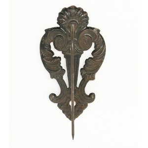May include: A black cast iron wall hook with a decorative scroll design. The hook has a pointed end and is designed to hold a variety of items.