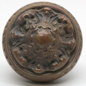 May include: A vintage brass door knob with an ornate floral design. The knob is round and has a raised centre with a detailed pattern.