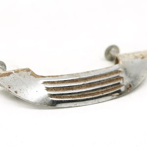 May include: A silver-toned metal cabinet pull with a curved shape and a ribbed design. The pull has two screw holes for installation.