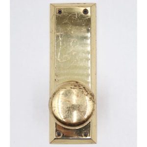 May include: A vintage brass door knob and plate set. The rectangular plate has rounded corners and four screw holes. The round knob is centered on the plate. The brass has a worn, aged appearance.