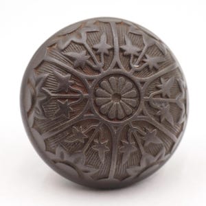 Könnte beinhalten: Dunkelbrauner, runder dekorativer Knopf mit einem komplizierten Blumen- und Sternmuster. Die Oberfläche des Knopfes ist mit geätzten Designs versehen, die eine zentrale Blume und sternförmige Elemente aufweisen. Die Gesamtästhetik ist Vintage oder antik.