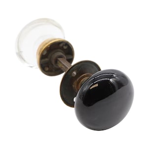 Op de afbeelding: Een zwarte keramische deurknoppen met een messing basis en een transparante glazen achterplaat.