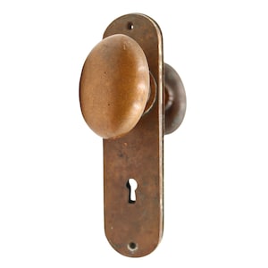 May include: An antique door handle set with a brown oval knob and a matching backplate. The backplate has a keyhole and mounting holes. The hardware is made of metal with a weathered finish, suggesting age and use.