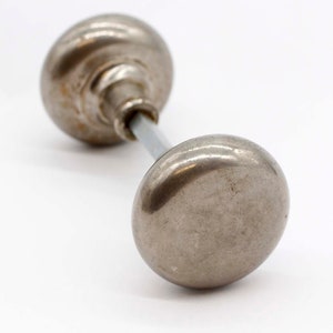 Może przedstawiać: Para antycznych srebrnych gałek drzwiowych z gładkim, lekko zużytym wykończeniem. Gałki są połączone metalowym prętem.