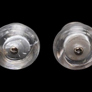 May include: Two clear glass bottle stoppers with a silver metal top. The stoppers are round and have a smooth surface.