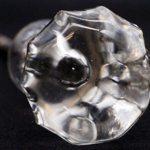 May include: A clear glass door knob with a faceted design. The knob has a small metal stem protruding from the back.