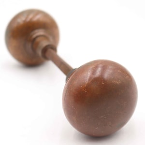 May include: A vintage, antique door knob with a brown, spherical design. The knob has a long, slender connecting rod and a smaller, decorative knob on the opposite end. The hardware is made of metal and has a worn, aged appearance.