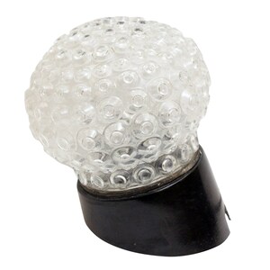 May include: A clear glass lampshade with a textured surface, resembling a sphere with many small circles. The lampshade is attached to a black base.