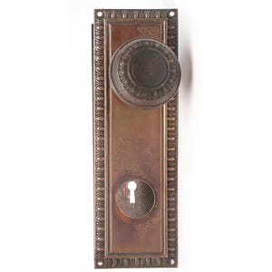 May include: A vintage brass door knob with a decorative border and a keyhole. The knob is round and has a raised design.