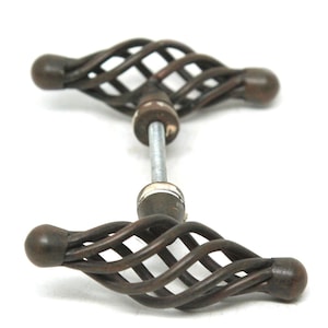 May include: Two antique bronze cabinet door handles. Each handle has a cage-like design with a central rod and rounded ends. The handles are set against a white background.
