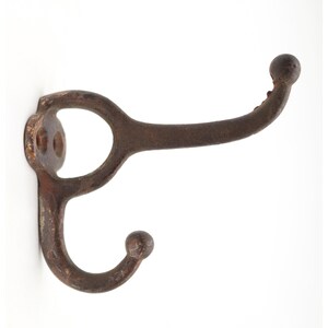 May include: A dark brown, weathered metal wall hook featuring a dual-prong design with a circular mounting plate. The hook has a textured, aged finish with visible signs of oxidation and two rounded tips at the ends of the curved arms.