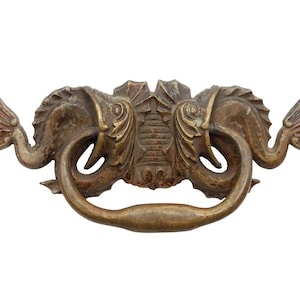 May include: A brass drawer pull with a decorative design of two stylized seahorses facing each other. The pull has a curved handle and a detailed, ornate design.