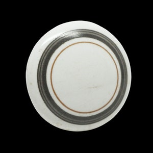 May include: A white ceramic plate with a concentric circle design in black and brown.